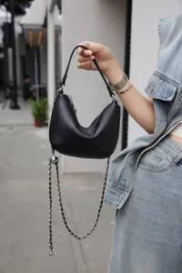 Detail view of black leather mini hobo shoulder bag with chic metal chain strap outdoors.