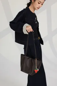 Close-up of dark brown leather tote bag featuring a cute strawberry charm and strap.