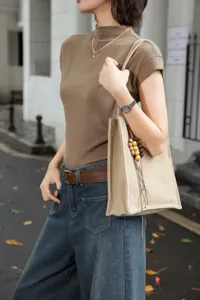 Detail shot of a minimalist genuine leather tote bag with bead charm, worn on shoulder.