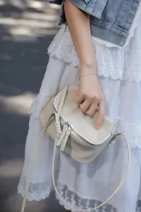 Detail view of mini leather crossbody bag, elegant beige cowhide design with zipper.