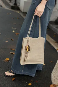 Detail shot of a minimalist beige leather tote bag with a charming bead pendant, outdoor.