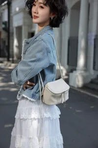 Detail view of a stylish minimalist white leather crossbody bag worn by a model outdoors.