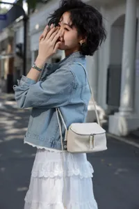 Close-up detail of white genuine leather mini crossbody bag with double zipper and strap.