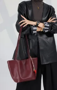 Detailed shot of a burgundy leather tote bag with double straps and a cute strawberry charm.