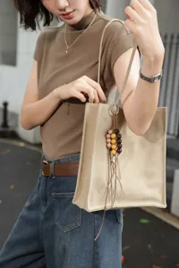 Minimalist genuine leather tote bag detail, featuring stylish wooden bead charm and large capacity.