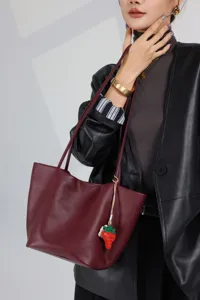 Detailed view of genuine leather burgundy shoulder bag with cute strawberry charm and strap.