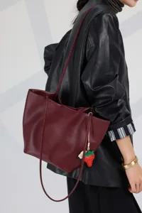 Burgundy leather tote bag detail showing soft cowhide texture and cute strawberry charm.
