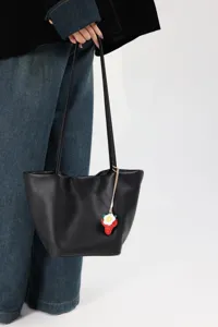 Black leather bucket bag detail showing soft texture and cute strawberry pendant accessory.