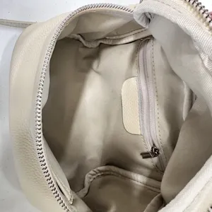 Detailed interior view of minimalist beige leather crossbody bag with zipper pocket and lining.