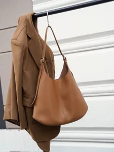 Detail shot of brown leather hobo shoulder bag hanging with a coat against modern architectural wall.