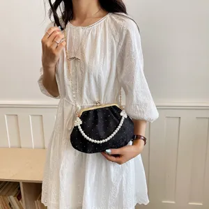 Vue détaillée du sac à main coquillage plissé noir avec poignée en perles et chaîne dorée.