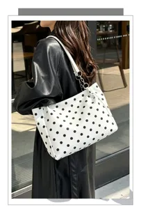 Gros plan détaillé du sac à main d'épaule blanc à pois noirs porté par le modèle.