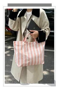 Detailed view of the casual pink canvas tote bag showing striped pattern and double handles in a street scene.
