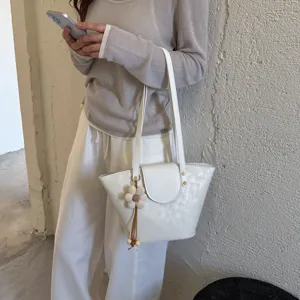 White minimalist shoulder tote bag detail view with elegant flower pendant charm accessory.