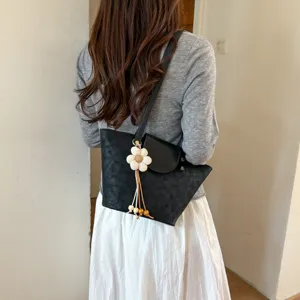 Detailed view of women black shoulder tote bag with cute white flower charm on model.