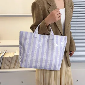 Detail view of a light purple striped tote bag with large capacity, held by a model indoors.
