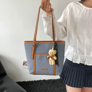 Detail shot of women casual tote shoulder bag featuring cute bear pendant and ribbon accessory.