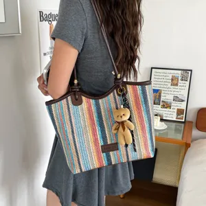 Colorful woven tote bag detail showing vibrant stripes, brown leather trim, and cute bear charm.