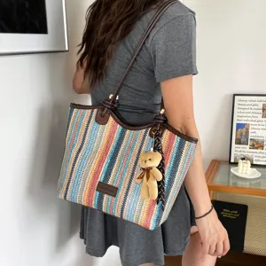 Close-up detail of the colorful straw woven tote bag featuring a cute bear plush pendant.