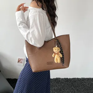 Brown PU leather shoulder tote bag detail shot featuring cute bear pendant and chic ribbon.