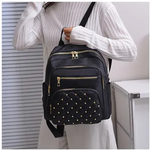 Close-up of black nylon backpack with quilted design, gold studs, and multiple zipper pockets.