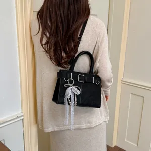 Detail view of stylish black shoulder bag featuring chic belt buckle and lace pearl pendant.