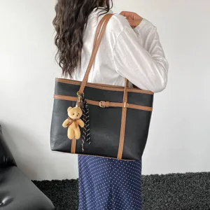 Detail view of a retro large capacity black tote bag with brown straps and cute bear charm.