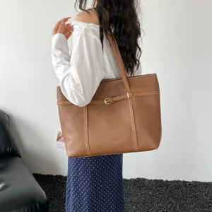 Detail view of the vintage brown tote bag showing vertical straps and metal buckle decoration.