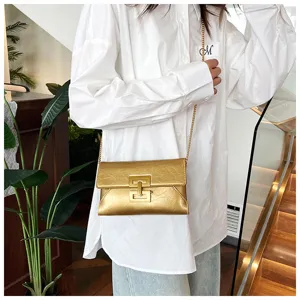 Gold metallic crossbody bag detail featuring unique geometric metal clasp and chain strap.