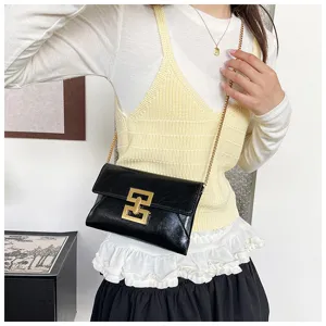Detail shot of a sleek black crossbody chain bag worn by a model, featuring a gold clasp.
