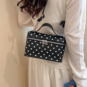 Detailed view of the black and white polka dot vanity handbag with top handle and shoulder strap.