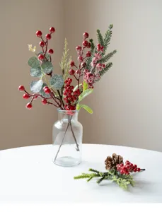 Detailed shot of artificial Christmas berry and pine needle branches in a clear glass vase.