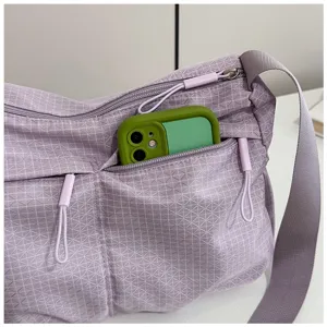 Close-up detail of a light purple grid nylon crossbody bag pocket with a green phone inside.