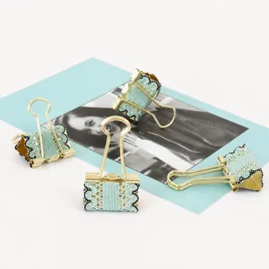 Detailed view of gold metal binder clips featuring elegant light blue lace trim, perfect for journaling.