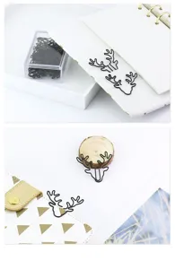 Close-up of cute black deer shaped paper clips used as creative bookmarks in a white notebook.
