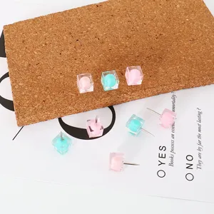 Gros plan de punaises carrées en résine, épingles pastel rose et bleu pour mur photo.