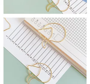 Detailed close-up view of cute golden cat-shaped paper clips resting nicely on a planner.
