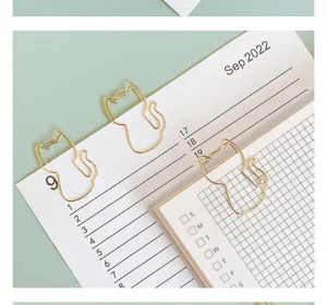 Detail shot of cute gold cat shaped paper clips clipped on planner, creative stationery.
