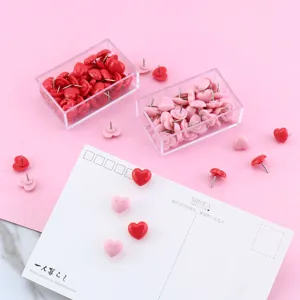 Cute pink and red heart-shaped push pins set with clear plastic storage box for office.