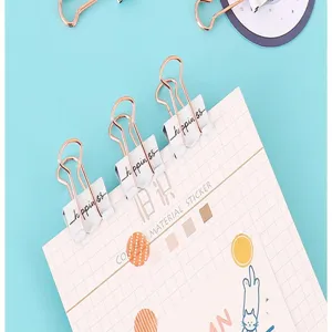 Primer plano de clips de carpeta creativos de oro rosa y blanco de 19 mm en papel cuadriculado.