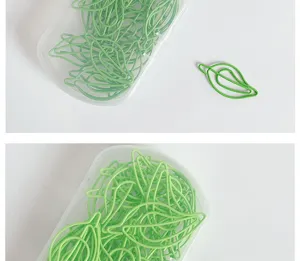 Close-up detail of green leaf shaped metal paper clips in a clear box for office use.
