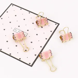 Detail view of cute gold metal binder clips with pink fabric and black lace trim for journaling.