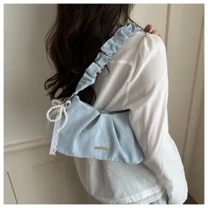 Detail view of the light blue pleated underarm bag with elegant pearl bow pendant design.