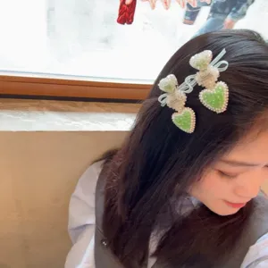 Gros plan sur la pince à cheveux cœur en strass vert menthe avec nœuds en perles.
