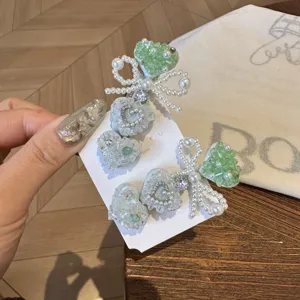 Détail de pince à cheveux cœur en pierre menthe avec nœud de perles blanches et strass.
