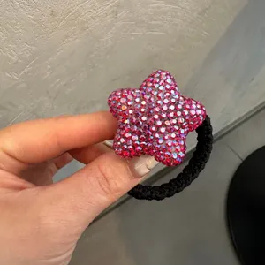 Detail en gros plan d'un elastique a cheveux etoile en strass brillant avec bande noire.