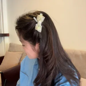 Detail shot of a mint green organza bow hair clip with rhinestone accent, worn in hair.