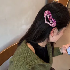 Vue de détail de la pince à cheveux cœur en strass rose étincelant dans les cheveux sombres.
