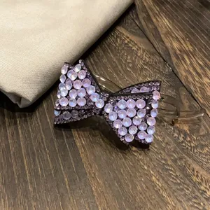 Vue détaillée de la pince à cheveux nœud en strass, ornée de cristaux violets scintillants.