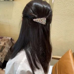 Vue détaillée d'une pince à cheveux triangulaire scintillante portée sur des cheveux sombres.